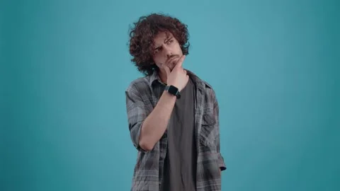 The young, curly-haired hipster thinks, looking to the right with his hand on Stock Footage 152791504