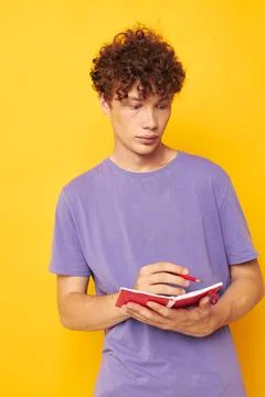 Young curly-haired man notepad with pen learning emotions yellow background Foto stock