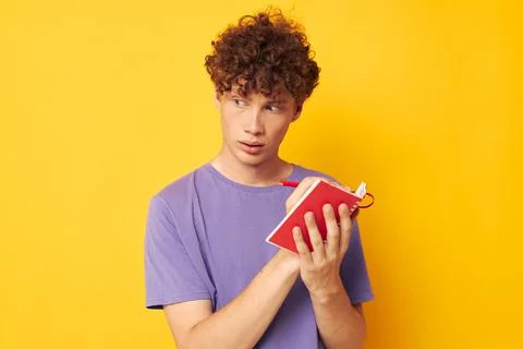 Young curly-haired man notepad with pen learning emotions yellow background Foto stock