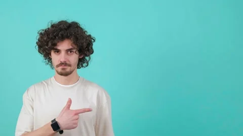 Young curly haired man is pointing to the left and showing the thumb up gesture Stock Footage 155809996