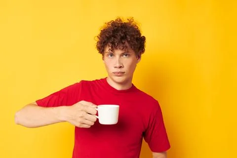 Young curly-haired man in a red T-shirt with a white cap in his hands isolated Fotos Stock