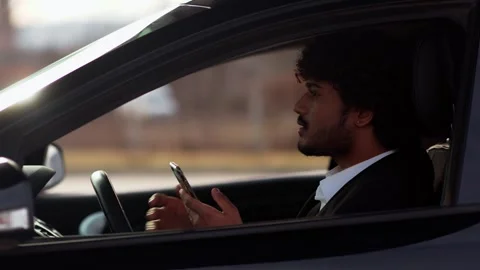 A young curly-haired man sits in a car and honks to the cars ahead. A guy in a Stock Footage 242609687