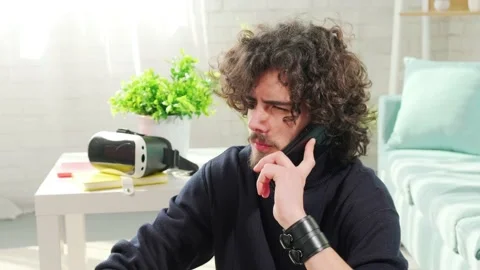Young curly haired man talking on phone while sitting on floor near sofa. Stock Footage 151539484