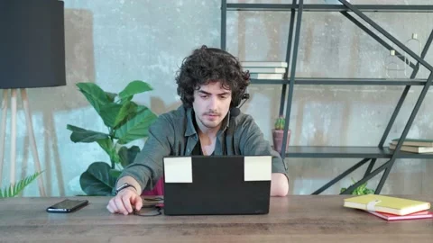 Young curly haired man using laptop computer with headset to talking online. Stock Footage 155807062