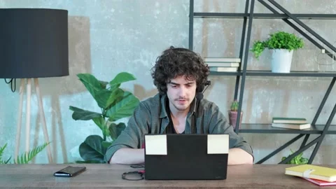 Young curly haired man using laptop computer with headset to talking online. Stock Footage 158450497