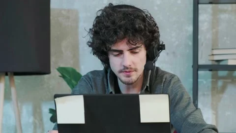 Young curly haired man using laptop computer with headset to talking online. Stock Footage 165286436