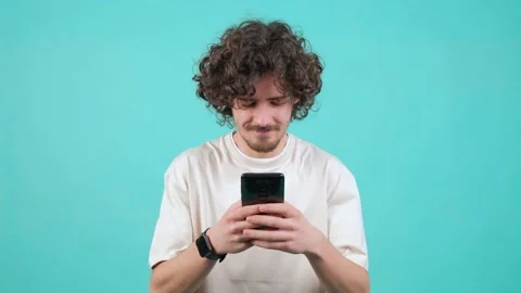 Young curly haired man watching a funny video on smartphone. Stock Footage 151285718