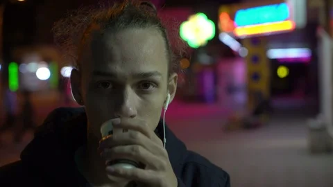 Young curly man drinks tea on the street at night, neon light 1 Stock Footage 96060339