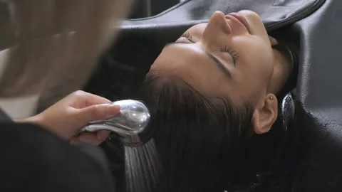 Young customer sleep on bed to wash hair by salon worker spraying her hair. Stock Footage