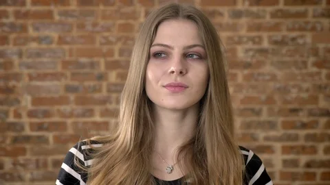 Young cute blonda is watching at camera suspiciously, brick background Video stock 92312810