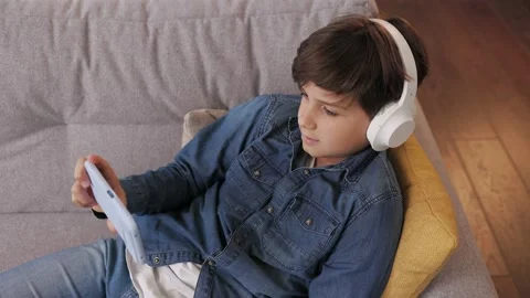 Young cute boy holding smartphone sitting at home. Teenager wearing earphones 스톡 동영상 213282931