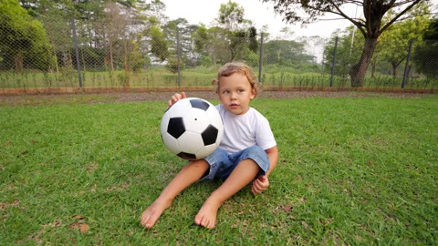 Young cute boy sitting on grass holding soccer ball, portrait shot Stock Footage 310528569