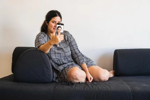 Young cute brunette girl takes herself a selfie with her smartphone while sit Stock Photos