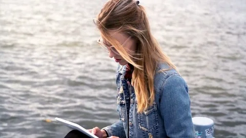 Young cute girl with tablet computer sitting close to the river 스톡 동영상 81862390