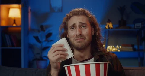 Young cute guy crying and wiping tears with paper napkin while sitting on sofa Stock-Footage 128974239