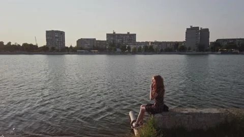 Young cute lady daydreaming while sitting on concrete parapet city waterfront Stock Footage 159632872