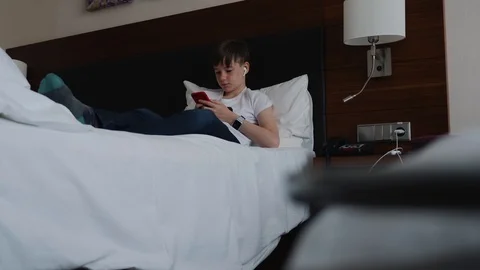 Young cute young man lying on a white bed and looking for something in the 動画素材 115069297
