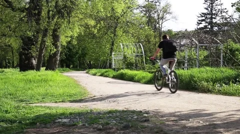 Young cyclist rides through the park on white cross-country bike Stock Footage 52134644