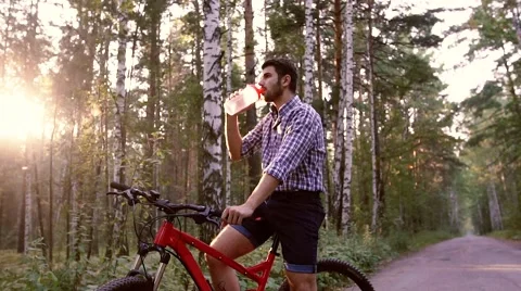 Young cyclist sitting on his bicycle and drinking water Stock Footage