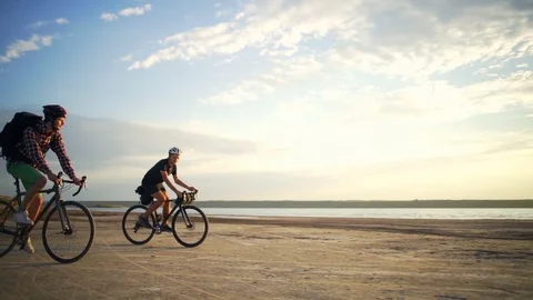 Young cyclists rides together helmets sand seaside dawn slow motion rapid Video stock 78059622