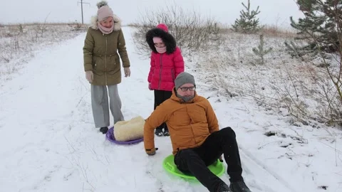 A young dad in glasses gets on a sled and tries to push off with his feet. Video stock 300284757