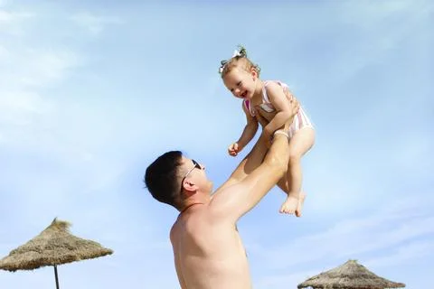 A young dad holds his tiny daughter above him against the sky on the beach Foto stock