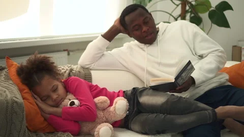 Young dad reading book and little daughter lying on sofa in apartment room spbd. Stock Footage 172461994