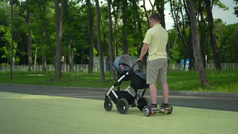 A young dad walks with a stroller on a hoverboard in the park. A modern dad on a Stock Footage 203856665