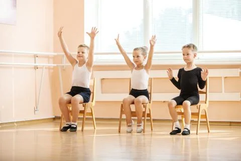 Young dancers playing or doing exercise while sitting on chairs Stock Photos