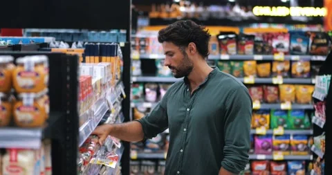 Young dark-haired bearded Caucasian man in casual clothes buys goods, reads the Stock Footage 218566282