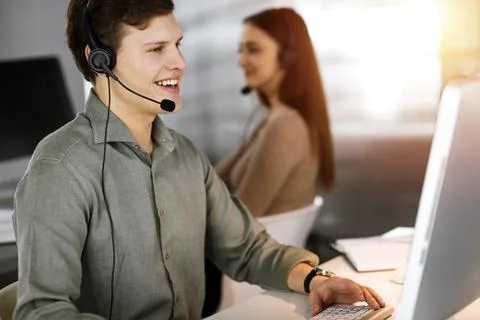 Young dark-haired guy in a green shirt and headsets is talking to a client Stockfoto's
