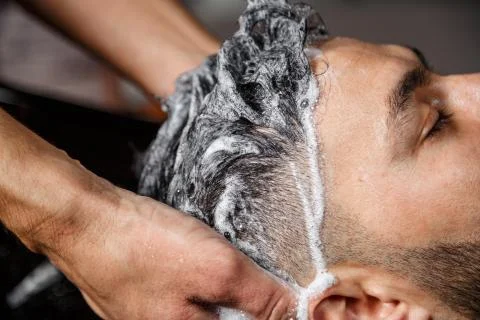 A young dark-haired guy of Indian or Asian appearance in a Barber shop on a b Stock Photos