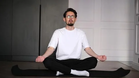 Young dark-haired man practicing yoga at home early in the morning on a mat Stock-Fotos