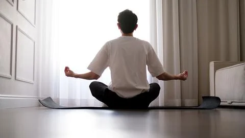 Young dark-haired man practicing yoga at home early in the morning on a mat Stock-Fotos