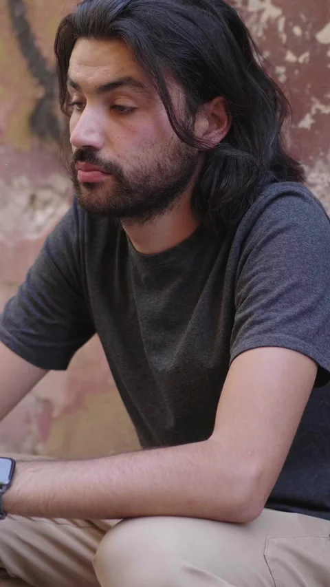 Young dark-haired man sits outside in deep thought, reflecting on life Stock Footage 285540487