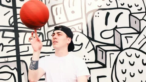Young dark-haired man with tattoo in a cap twists a basketball on his finger. Stock-Footage 144688206