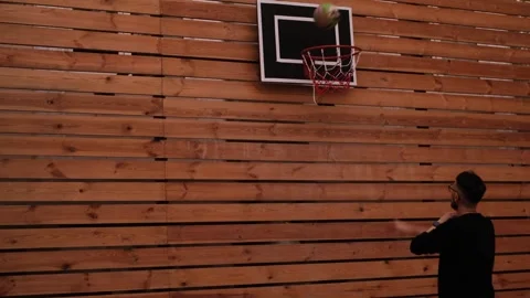 A young dark-haired man throws a basketball into the hoop on an outdoor wooden c Stock Footage 321195874