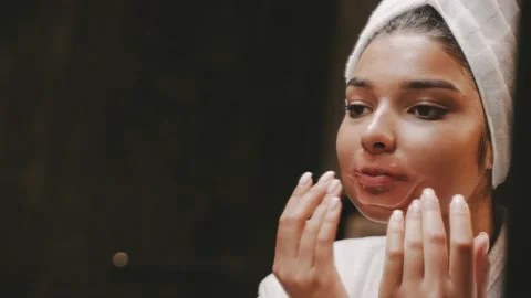 A young dark-skinned brunette in a dressing gown uses a patch for lips Morning Stock Footage 162498744