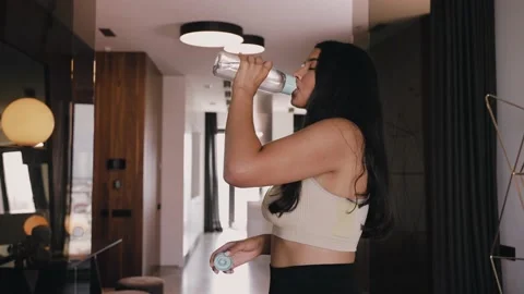 Young dark-skinned brunette drinks water from a bottle in beautiful interior 스톡 동영상 161326763