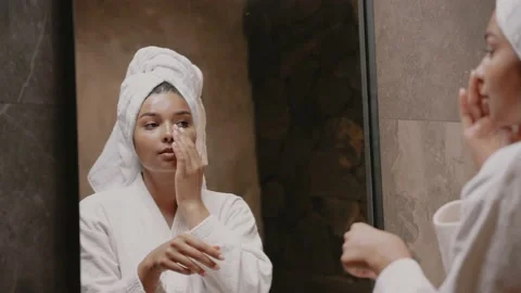 Young dark-skinned brunette in front of a mirror in a dressing gown. Skin care Video stock 162497622