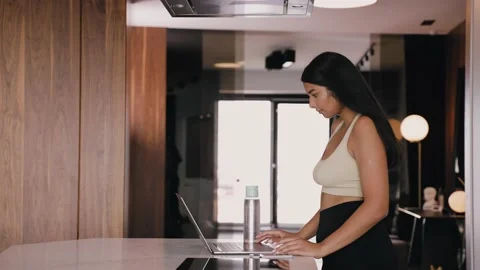 A young dark-skinned brunette in kitchen is typing on a laptop. Work from home Vídeo Stock 161387228