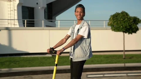 Young dark-skinned guy ride electric scooter on square at sunny summer day Stock Footage 115982669