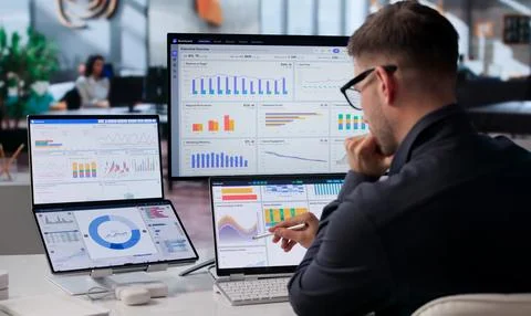 Young Data Analyst Studies Financial KPIs On Dual Screens. Stock Photos