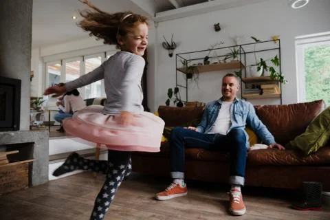 Young daughter dancing around while father happy spectates on sofa of living Stock Photos