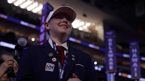 A young delegate in a white cap smiles and applauds near the Iowa, Delaware and Stock-Footage 345271822