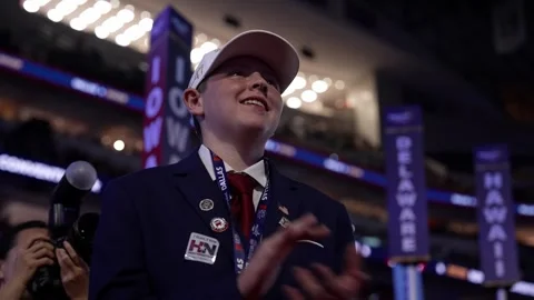A young delegate in a white cap smiles and applauds near the Iowa, Delaware and Stock Footage 345271844