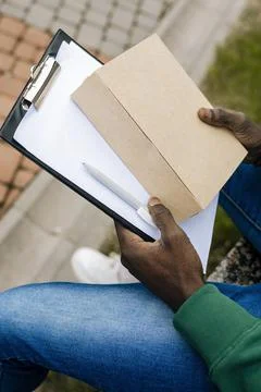 A young delivery man holds a box and coffee in his hands. Stock Photos