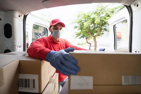 Young delivery man loading boxes in van truck while wearing face mask and gloves Stock Photos