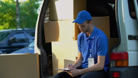 Young deliveryman writing parcel distribution report and smiling, sitting in van Stock Footage 91244586