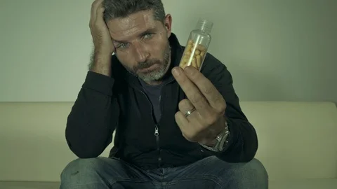 Young depressed and dramatic man holding pills sitting on couch Stock Footage 113534809